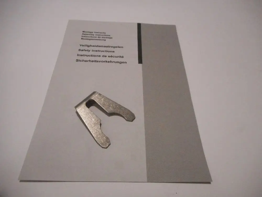 Metallic clip auf einer Anleitung, die Sicherheitshinweise und Montageanleitungen von Remeha enthält. Der Clip ist zur Befestigung von Komponenten gedacht.